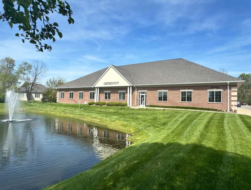 Large brick building of Ortho Indy office in Fishers, IN, with a serene pond in front